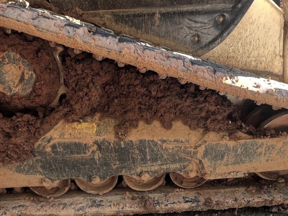 Before, close-up: loader track packed solid with red clay