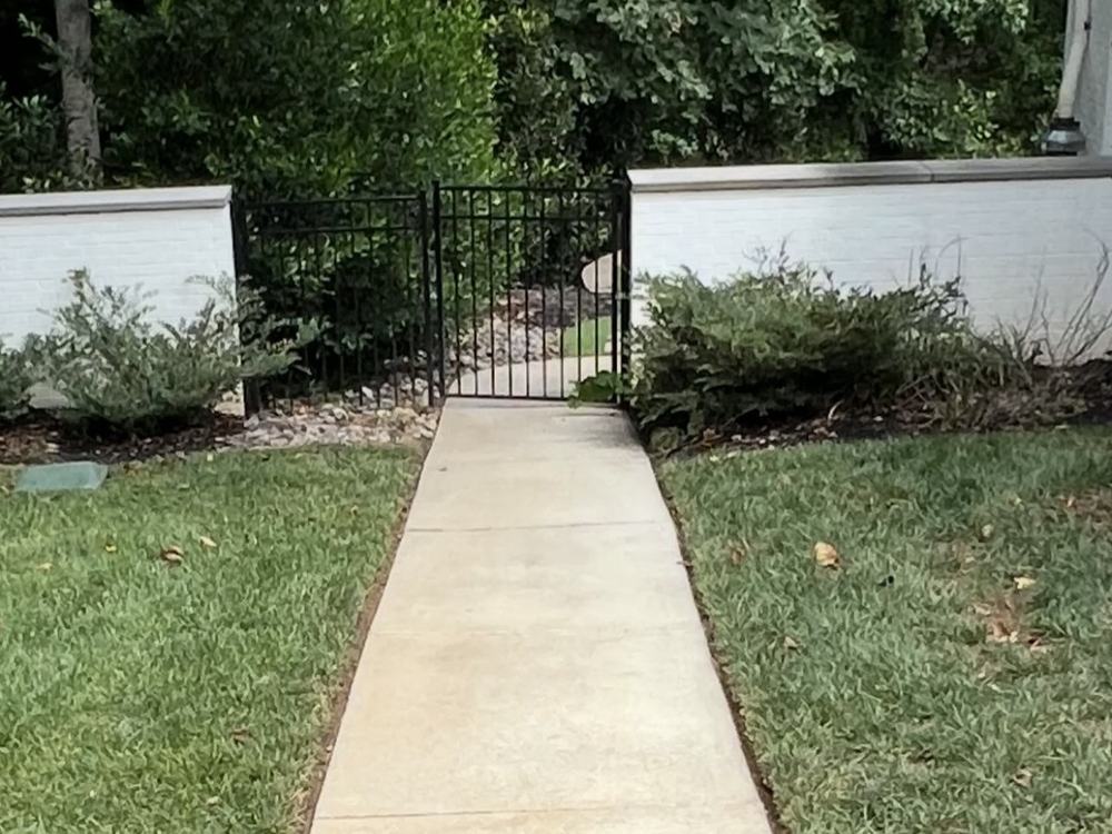 After: bright, clean concrete walkway leading to the same black iron gate